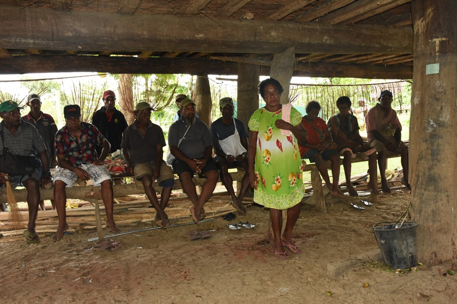 Woman leading a community meeting with village elders seated in a traditional meeting house in Timbunke, Papua New Guinea.